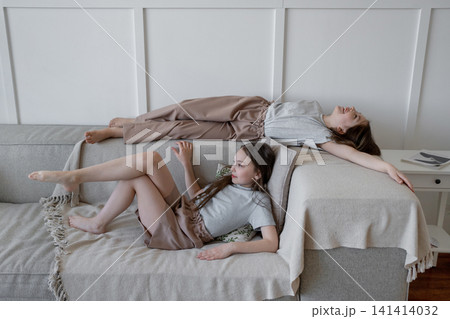 Two girls lying sideways on bed with arms stretched, relaxing and smiling in sunny bedroom. Lying, bed, arms, relaxing, girls, sunny. Two girls lying sideways on bed with arms stretched, relaxing and smiling in sunny bedroom. Lying, bed, arms, relaxing, girls, sunny. 141414032