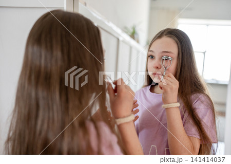 Preteen girls standing close together and smiling, using makeup brush in front of mirror at bedroom. Makeup, mirror, smile, girls, bedroom, beauty. 141414037