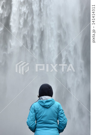 Hiker standing before the immense Skogafoss waterfall, Iceland 141414311