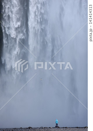 A hiker standing below the towering Skogafoss waterfall, Iceland A hiker standing below the towering Skogafoss waterfall, Iceland 141414313
