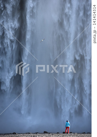 A hiker standing below the towering Skogafoss waterfall, Iceland A hiker standing below the towering Skogafoss waterfall, Iceland 141414314