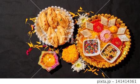Diwali celebration flat lay with lit clay diya sweets and marigolds on black background Diwali celebration flat lay with lit clay diya sweets and marigolds on black background 141414361