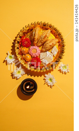 Diwali festive thali with traditional Indian sweets and lit diya on yellow background Diwali festive thali with traditional Indian sweets and lit diya on yellow background 141414426