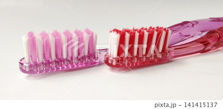 A close-up photo of the heads of pink and red manual toothbrushes. A close-up photo of the heads of pink and red manual toothbrushes. 141415137