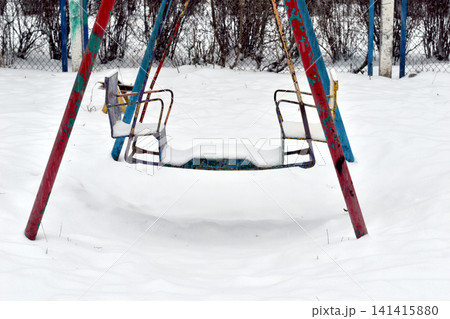 There is snow on the children's swings. There is snow on the children's swings. 141415880