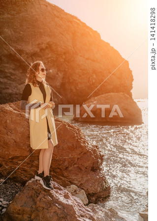Woman beach sunset enjoying the view from rocky cliffs over the ocean during golden hour Woman beach sunset enjoying the view from rocky cliffs over the ocean during golden hour 141418298