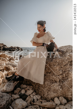 Woman dress cat smiling lady in vintage white gown sitting on a coastal rock with her black pet 141418313