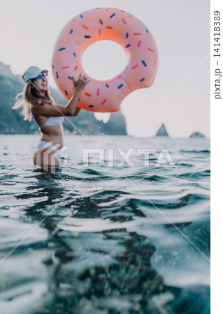 Woman, donut, inflatable. Happy woman holds a donut inflatable in the sea, enjoying summer vacation with copy space. 141418389