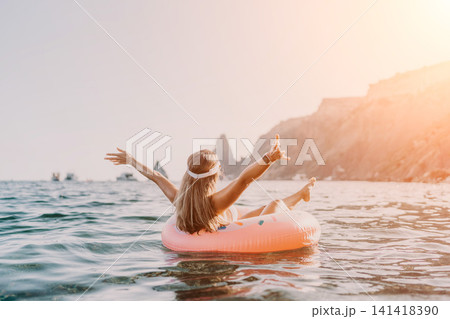 Woman, sea, vacation. Happy woman floating on inflatable ring at sea with arms outstretched, sunny cliff background. 141418390