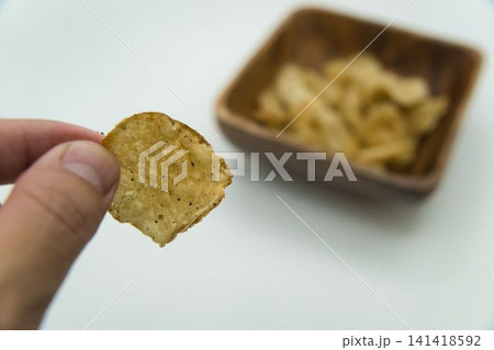 一枚のポテトチップスをつまむ手 一枚のポテトチップスをつまむ手 141418592