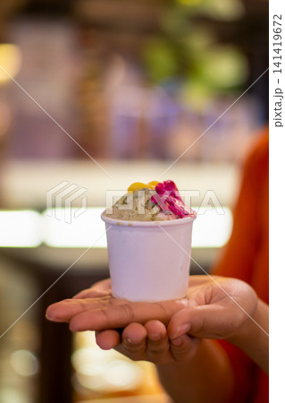 Artisan Gelato Served in Paper Cup Held by Customer Hand in Cozy Cafe Artisan Gelato Served in Paper Cup Held by Customer Hand in Cozy Cafe 141419672