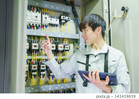 タブレットを持って制御盤の点検をする若い日本人男性作業員　撮影協力：学校法人電波学園　東京電子専門学 141419839