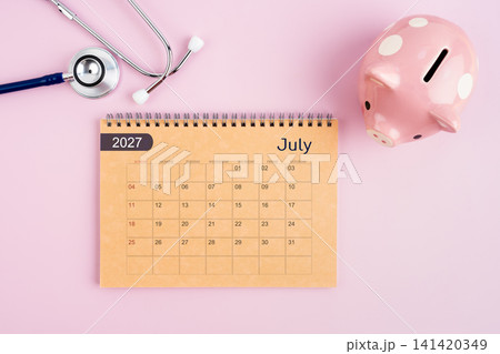 July 2027 desk calendar and stethoscope with piggy bank. Savings for Health concept. July 2027 desk calendar and stethoscope with piggy bank. Savings for Health concept. 141420349