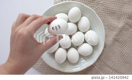 Woman's hand and a ceramic bowl with white eggs on a striped kitchen napkin. Healthy eating, keto and paleo diet Woman's hand and a ceramic bowl with white eggs on a striped kitchen napkin. Healthy eating, keto and paleo diet 141420942