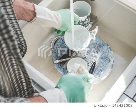Man in green rubber gloves washes dishes Man in green rubber gloves washes dishes 141421002