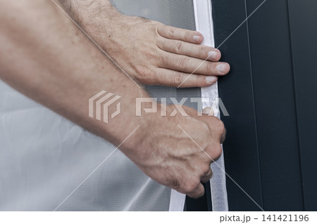 Hands adjusting a mosquito screen on hook and loop tape on a window frame, illustrating home maintenance and practical DIY work. Hands adjusting a mosquito screen on hook and loop tape on a window frame, illustrating home maintenance and practical DIY work. 141421196