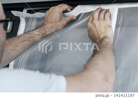Person securing a white magnetic mosquito screen into the frame of balcony door, illustrating precise home task and maintenance. 141421197