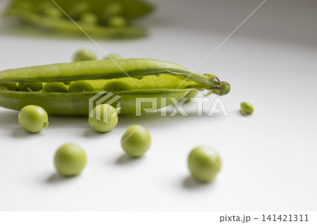 Fresh green peas in an open pod isolated on a white background. Close up shot of organic legumes, healthy food ingredient, raw vegetable, natural harvest, vegan nutrition, vegetarian eating concept. Fresh green peas in an open pod isolated on a white background. Close up shot of organic legumes, healthy food ingredient, raw vegetable, natural harvest, vegan nutrition, vegetarian eating concept. 141421311