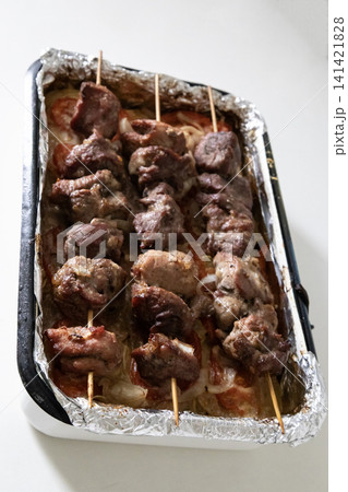 Baked meat skewers on wooden sticks placed in a baking tray over sliced tomatoes and onions, ready for serving delicious homemade barbecue meal, top view. Baked meat skewers on wooden sticks placed in a baking tray over sliced tomatoes and onions, ready for serving delicious homemade barbecue meal, top view. 141421828