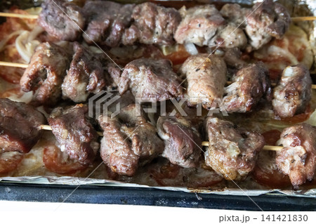 Baked meat skewers on wooden sticks placed in a baking tray over sliced tomatoes and onions, ready for serving delicious homemade barbecue meal, top view. 141421830