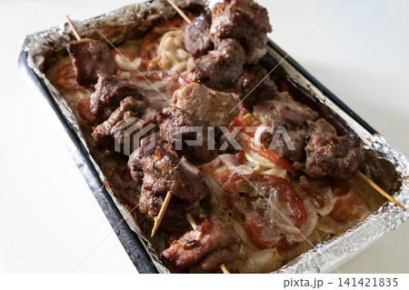 Baked meat skewers on wooden sticks placed in a baking tray over sliced tomatoes and onions, ready for serving delicious homemade barbecue meal, top view. Baked meat skewers on wooden sticks placed in a baking tray over sliced tomatoes and onions, ready for serving delicious homemade barbecue meal, top view. 141421835