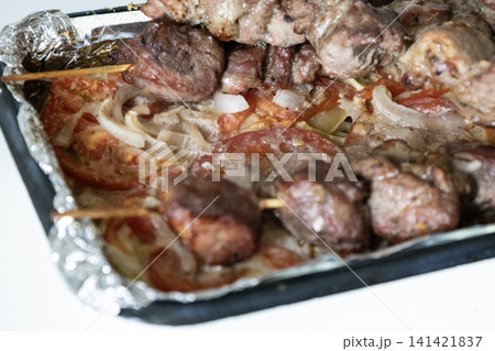 Baked meat skewers on wooden sticks placed in a baking tray over sliced tomatoes and onions, ready for serving delicious homemade barbecue meal, top view. Baked meat skewers on wooden sticks placed in a baking tray over sliced tomatoes and onions, ready for serving delicious homemade barbecue meal, top view. 141421837