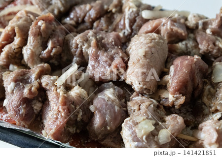 Raw marinated pork meat skewers on wooden sticks arranged in a baking tray with sliced tomatoes and onions, ready for cooking barbecue, top view. 141421851