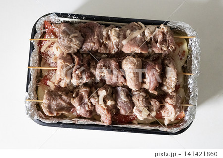 Raw marinated pork meat skewers on wooden sticks arranged in a baking tray with sliced tomatoes and onions, ready for cooking barbecue, top view. Raw marinated pork meat skewers on wooden sticks arranged in a baking tray with sliced tomatoes and onions, ready for cooking barbecue, top view. 141421860