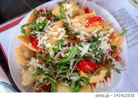 Naples, italy. December 30, 2024. Angioletti fritti, a neapolitan fried dough snack, topped with fresh arugula, vibrant cherry tomatoes, and grated parmesan cheese Naples, italy. December 30, 2024. Angioletti fritti, a neapolitan fried dough snack, topped with fresh arugula, vibrant cherry tomatoes, and grated parmesan cheese 141422038