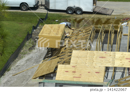 Builders working on roof construction of unfinished residential house with wooden frame structure in Florida suburban area. Housing development concept 141422067