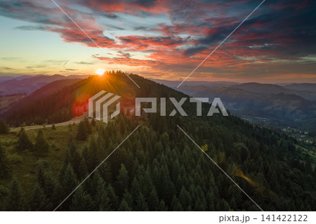 Beautiful landscape. Dramatic sunset over highland terrain. Dark pine forest illuminated with bright setting sun. Colorful nature of wild mountains Beautiful landscape. Dramatic sunset over highland terrain. Dark pine forest illuminated with bright setting sun. Colorful nature of wild mountains 141422122
