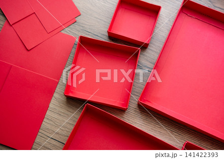 Lids from a red collapsible gift box gathered on a wooden table. Preparing a surprise. Lids from a red collapsible gift box gathered on a wooden table. Preparing a surprise. 141422393