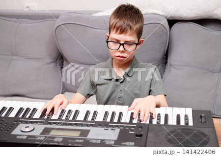 A boy with glasses and hearing aids is learning to play the synthesizer. The schoolchild has a hearing disability. 141422406
