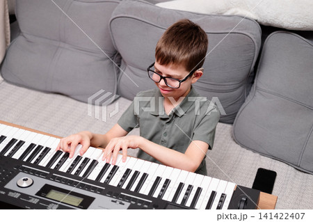 A boy with glasses and hearing aids is learning to play the synthesizer. The schoolchild has a hearing disability. A boy with glasses and hearing aids is learning to play the synthesizer. The schoolchild has a hearing disability. 141422407