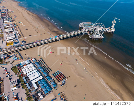 Beautiful high altitude aerial panoramic perspective of an iconic sea pier with a ferris wheel bungee tower and beach resort clubs on a sandy coast under a blue sky Beautiful high altitude aerial panoramic perspective of an iconic sea pier with a ferris wheel bungee tower and beach resort clubs on a sandy coast under a blue sky 141422579
