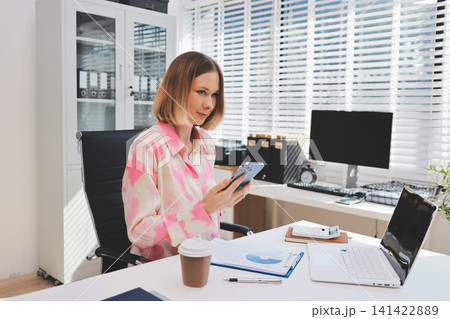 Confident and Composed: A professional businesswoman exudes confidence and composure as she works on her laptop, surrounded by the vibrant energy of a modern office space. Confident and Composed: A professional businesswoman exudes confidence and composure as she works on her laptop, surrounded by the vibrant energy of a modern office space. 141422889