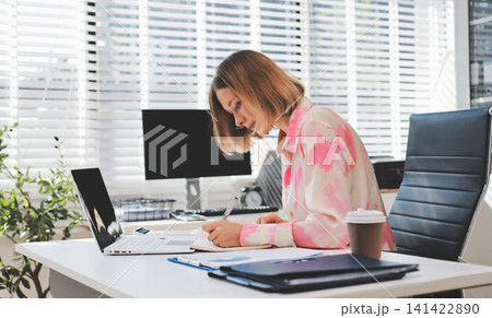 Confident and Composed: A professional businesswoman exudes confidence and composure as she works on her laptop, surrounded by the vibrant energy of a modern office space. Confident and Composed: A professional businesswoman exudes confidence and composure as she works on her laptop, surrounded by the vibrant energy of a modern office space. 141422890