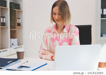 Young businesswoman smiling as she works on a laptop sitting in an modern office Young businesswoman smiling as she works on a laptop sitting in an modern office 141422893