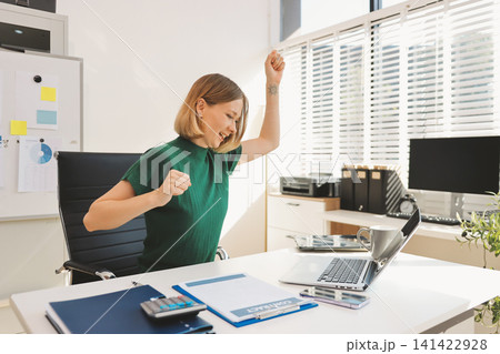 Young beautiful businesswoman works in the office with a laptop. Success Young beautiful businesswoman works in the office with a laptop. Success 141422928