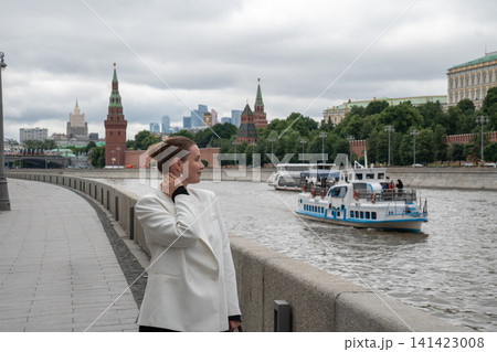 Smiling woman points toward Kremlin while standing on Sofiyskaya Embankment beside Moscow River. Travel, sightseeing, urban lifestyle, architecture, city exploration, tourism, confidence Smiling woman points toward Kremlin while standing on Sofiyskaya Embankment beside Moscow River. Travel, sightseeing, urban lifestyle, architecture, city exploration, tourism, confidence 141423008