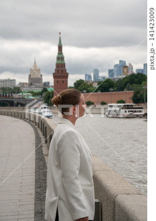 Woman looks across Moscow River from Sofiyskaya Embankment toward Kremlin and Moscow City skyline on cloudy day. Urban lifestyle, travel, reflection, architecture, sightseeing, city exploration Woman looks across Moscow River from Sofiyskaya Embankment toward Kremlin and Moscow City skyline on cloudy day. Urban lifestyle, travel, reflection, architecture, sightseeing, city exploration 141423009