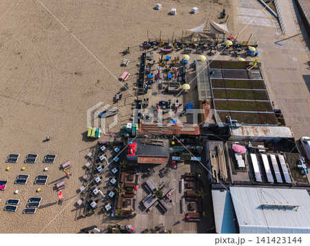 Beautiful top down high altitude aerial panoramic perspective of seaside beach clubs with outdoor patio terraces wooden furniture sunbeds and green roofs under bright sunlight Beautiful top down high altitude aerial panoramic perspective of seaside beach clubs with outdoor patio terraces wooden furniture sunbeds and green roofs under bright sunlight 141423144