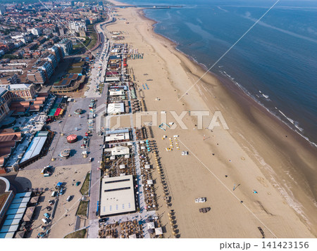 Beautiful high altitude aerial panoramic perspective of a long sandy beach promenade with beach clubs and dense urban resort city along the North Sea coast under a blue sky Beautiful high altitude aerial panoramic perspective of a long sandy beach promenade with beach clubs and dense urban resort city along the North Sea coast under a blue sky 141423156