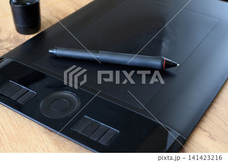 Digital stylus rest on a black graphics tablet for digital drawing. Digital illustration process concept. Digital stylus rest on a black graphics tablet for digital drawing. Digital illustration process concept. 141423216