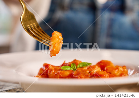 Gnocchi in tomato sauce lifted with fork above white plate garnished with basil 141423346