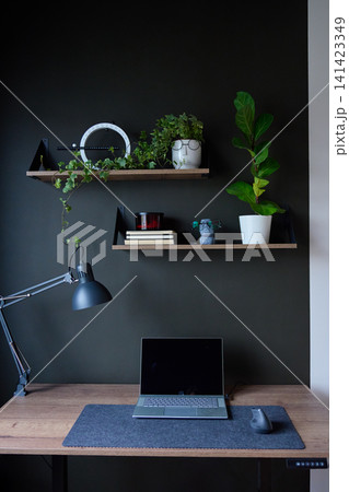 Modern home office with laptop on wooden desk, floating shelves and indoor plants against dark wall Modern home office with laptop on wooden desk, floating shelves and indoor plants against dark wall 141423349