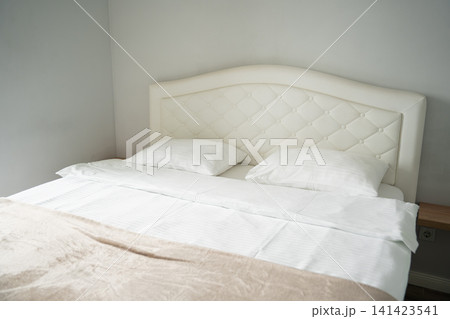 Minimalist bedroom with white upholstered headboard and simple bedding. Home decor interior design and real estate staging 141423541