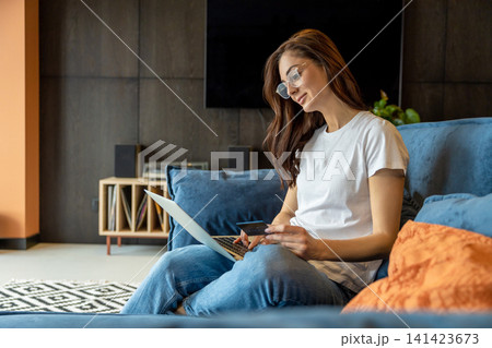 Smiling young woman with laptop in hands sitting on a sofa Smiling young woman with laptop in hands sitting on a sofa 141423673