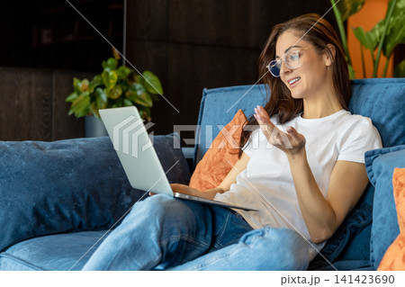 Woman in white tshirt and jeans on the sofa with a laptop in hands Woman in white tshirt and jeans on the sofa with a laptop in hands 141423690