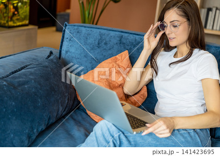 Young woman in eyeglasses working on a laptop and looking busy Young woman in eyeglasses working on a laptop and looking busy 141423695